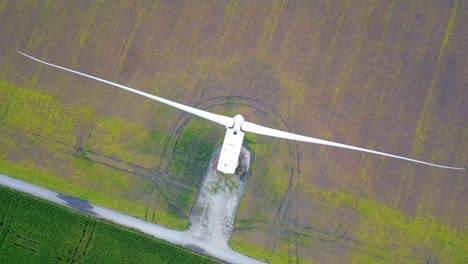 orbiting aerial view looking down at wind turbines spinning blades on green cultivated farmland field