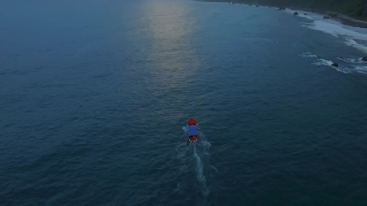 Aerial view of a blue and orange boat cruising a calm green caribbean sea