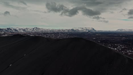 Malerische-Drohnenaufnahme-Des-Vulkans-Hverfjall,-Die-Den-Krater-Und-Das-Umliegende-Gelände-Mit-Einem-Berghintergrund-Einfängt