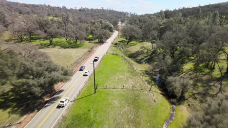 Drone-Siguiendo-La-Conducción-Del-Automóvil-A-Través-De-Un-Bosque-De-Robles-En-Colinas-Onduladas