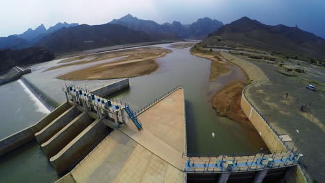 Aerial-view-of-spillway-of-a-dam,-Beautiful-majestic-mountains-in-the-back-of-the-dam