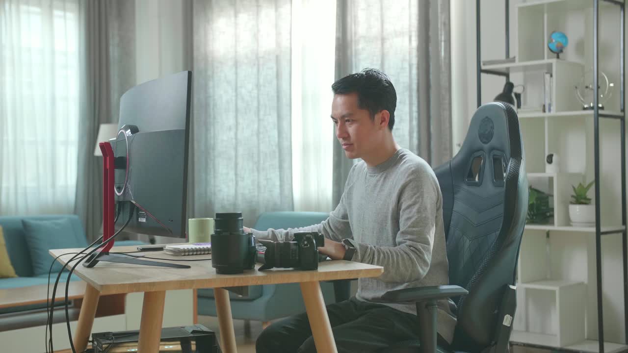 Asian Cameraman In Long Sleeved T-Shirt And Black Pants Using Desktop Computer For Working At Home.