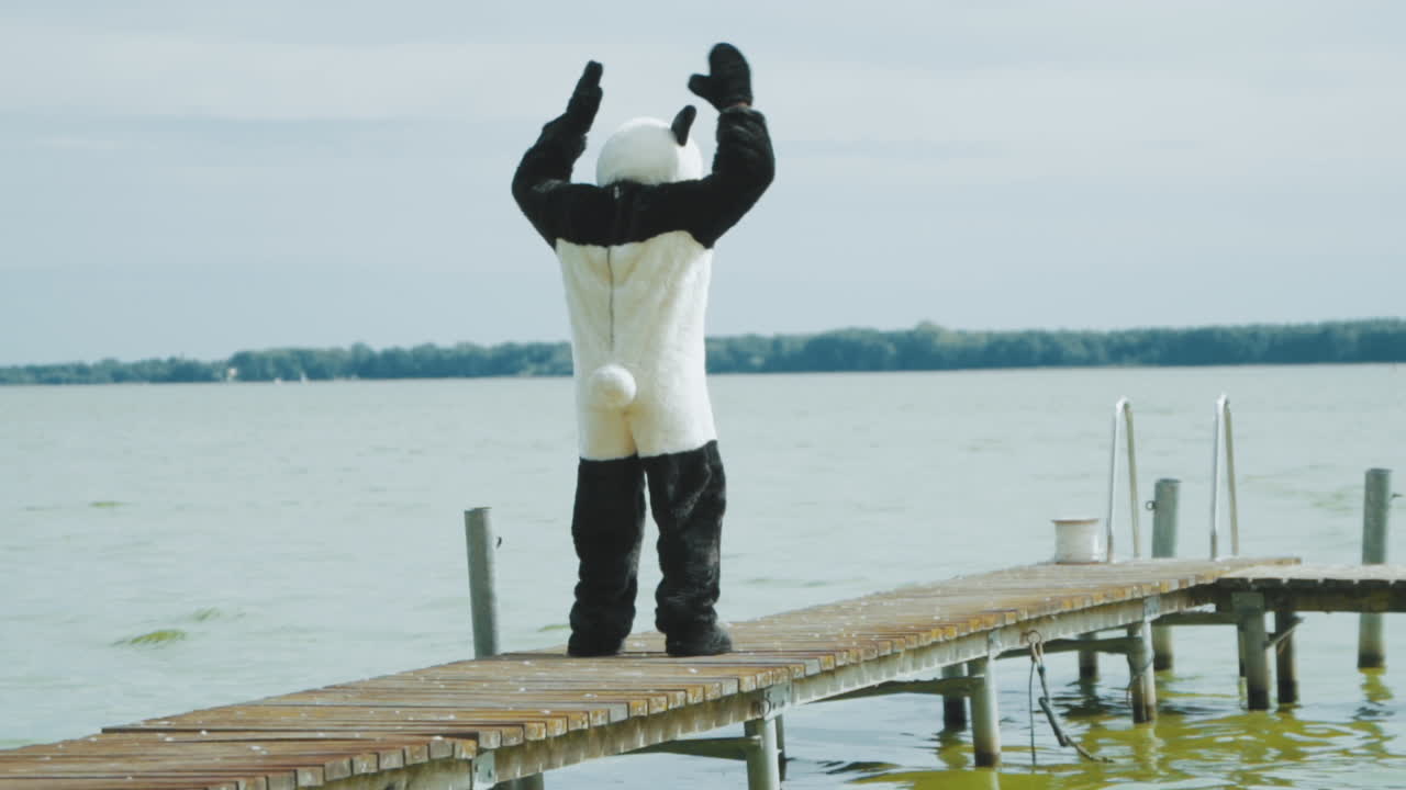 Wide shot from behind of a guy in Panda costume working out on a pier at a lake