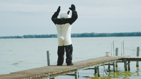 wide shot from behind of a guy in panda costume working out on a pier at a lake