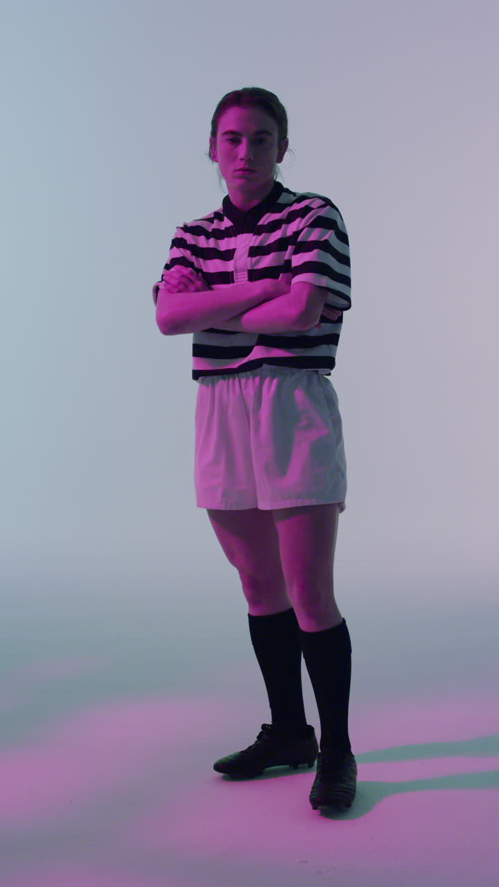 video vertical del retrato de una jugadora de rugby caucásica con los brazos cruzados sobre iluminación rosada