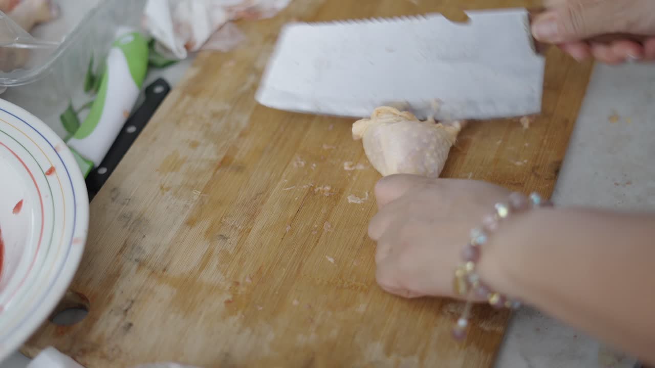 Preparing Raw Chicken on a Cutting Board with a Cleaver