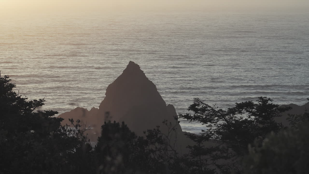 Sunset on the Califonia coastline over a large boulder in the ocean