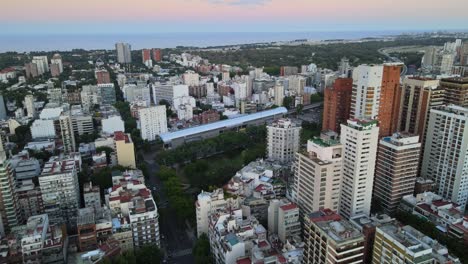 dolly in flying over barrancas de belgrano park and train station surrounded by buildings at sunset, buenos aires, argentina