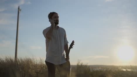 man talking on phone with guitar at sunset