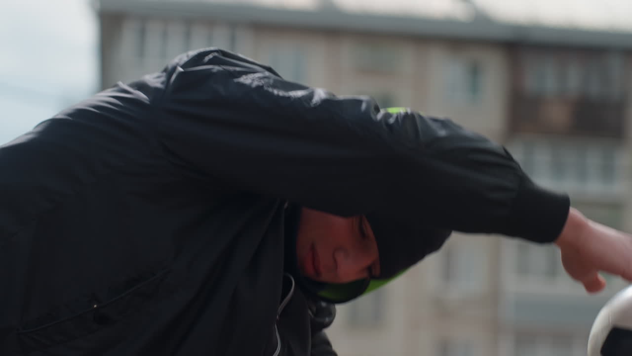 Joven portero caucásico estirándose para atrapar el balón con los brazos extendidos, gorro y chaqueta oscura, expresión concentrada y un apartamento urbano de fondo, primer plano del movimiento que muestra reflejos e intensidad de entrenamiento
