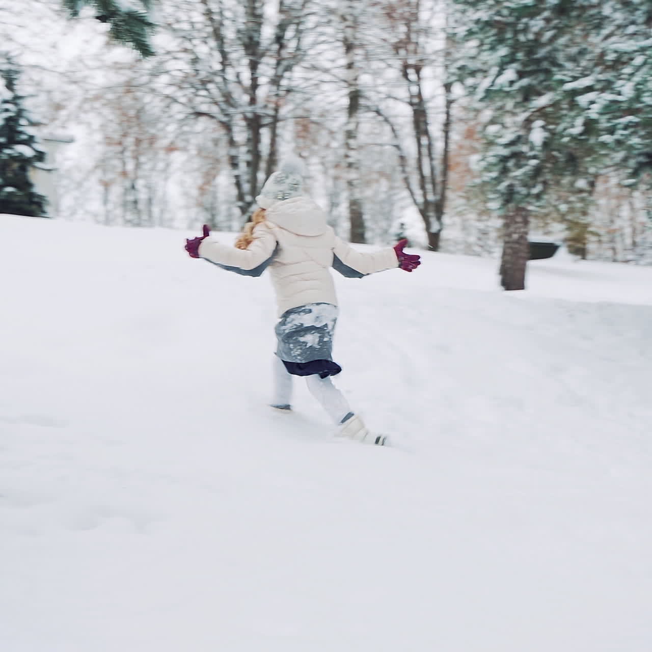 Little girl is running in the snow and falling into it in winter. Side view of a child who is having fun in cold season outdoors. Slow motion.