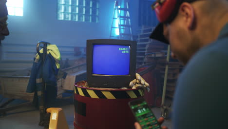 two men watching an old tv in a workshop while checking a smartphone