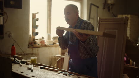 serious man preparing wooden plank for product indoors. man blowing out sawdust