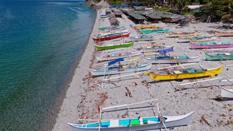 Lots-of-small-kayak-style-fishing-boats-lined-up-on-a-beautiful-white-sandy-beach-in-Mabua,-Philippines,-on-a-bright-sunny-day