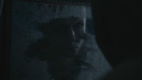 pale bald skinny man looks into the mirror in the creepy old bathroom at night