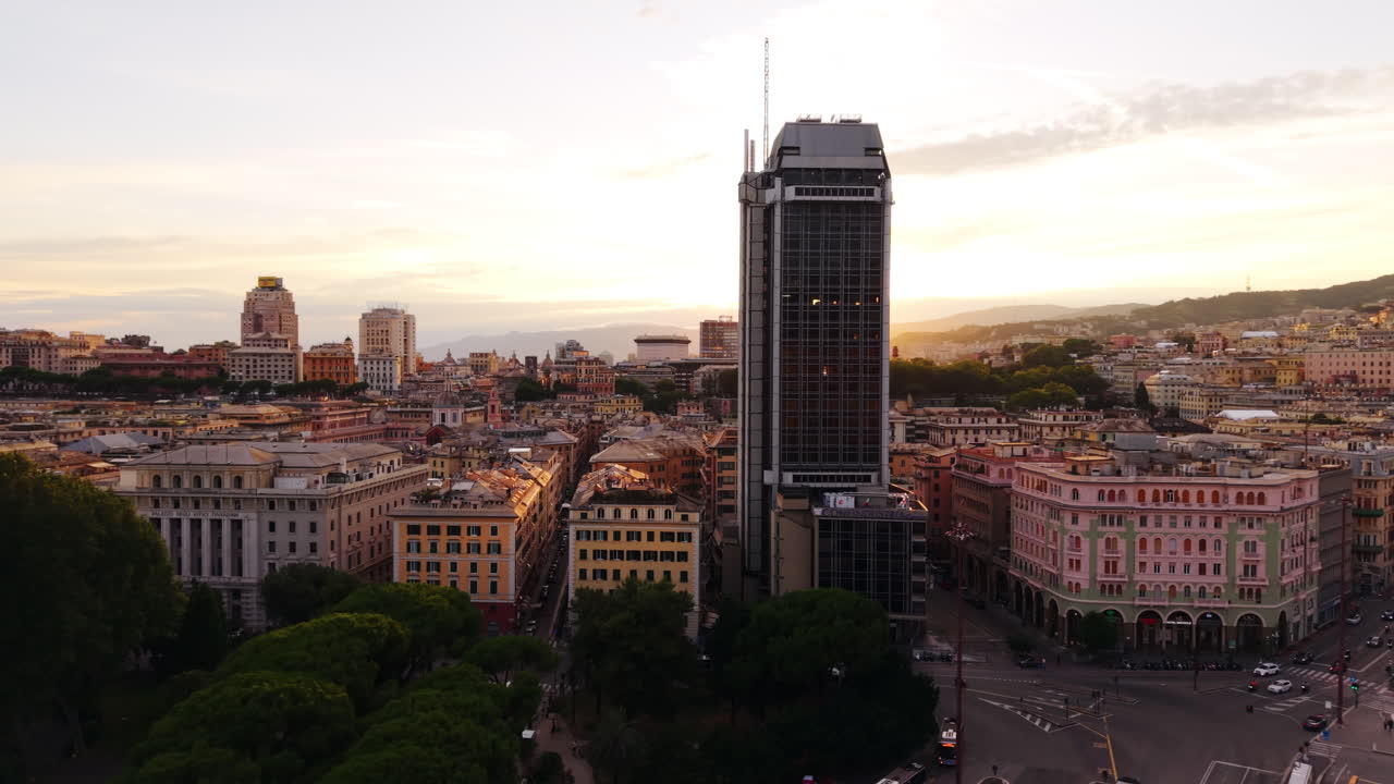 Drone panning shot of Torre San Vincenzo with Piazza Verdi, showing trees, historical buildings, and the cityscape at sunset