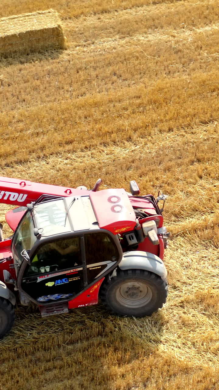 Tractor collecting bales of hay. Aerial view of tractor colecting on agricultural field. Vertical video