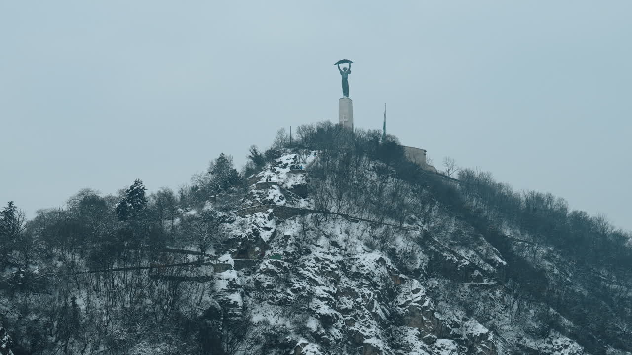 Vinterudsigt over monumentet for Daniel Bogdanich i Budapest, Ungarn. Scenen viser statuen under kolde vejrforhold med overskyet vejr, en sæsonbestemt atmosfære og statuen på en bakke.