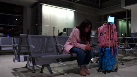 mujer espera su vuelo al lado del equipaje jugando con el teléfono mientras tose
