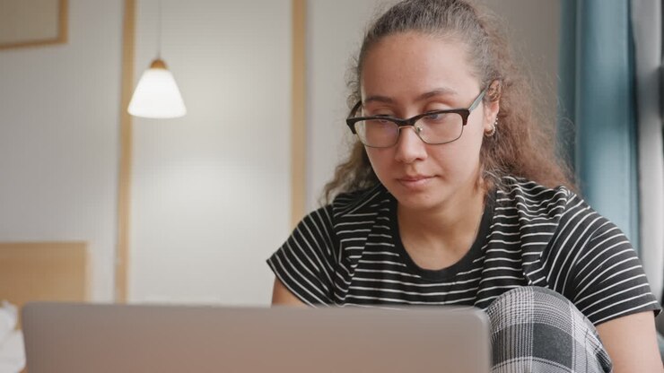 Ospite dell'hotel che lavora al portatile in camera, primo piano di donna concentrata alla postazione di lavoro accanto al letto sotto la luce calda di una lampada, che partecipa a riunioni video, risponde alle email e gestisce la routine di viaggio