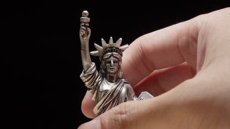 hand picking a little statue of liberty replica with black background