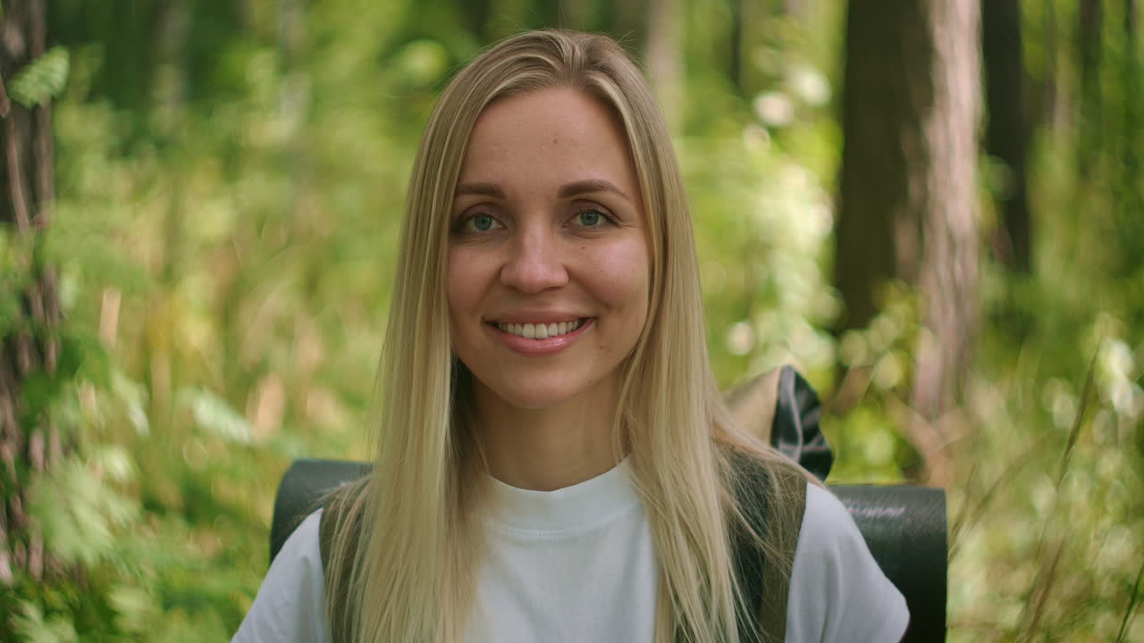 Portrait of a young woman traveler in the sun looking directly into the camera and smiling flirting Traveler with a backpack in the Park and in the woods in slow motion