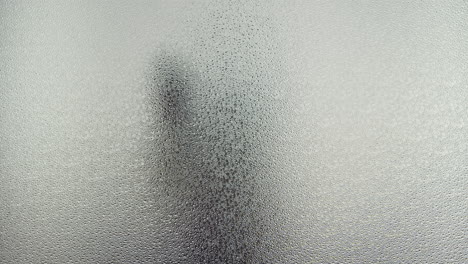 a female silhouette behind the frosted glass moves slowly and kiss the glass