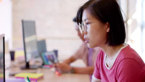 thoughtful asian female creative working at computer in casual office, slow motion