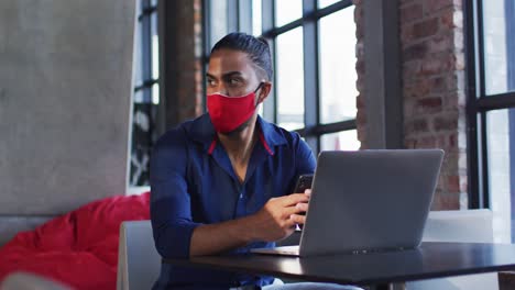 African-american-man-wearing-face-mask-sitting-in-cafe-using-laptop