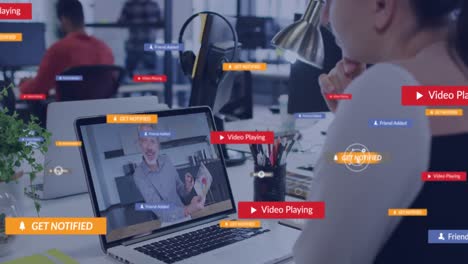 Animation-Von-Social-Media-Symbolen-Vor-Einer-Kaukasischen-Frau,-Die-Im-Büro-Einen-Videoanruf-Auf-Einem-Laptop-Führt