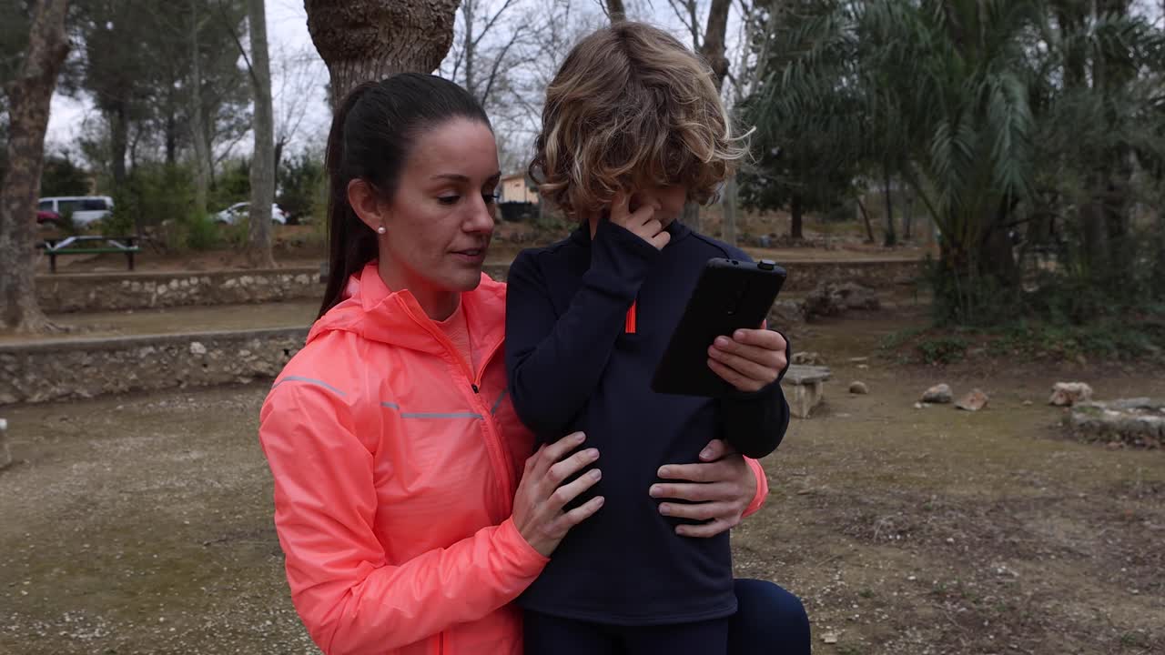 mujer deportiva sonriente con su hijo en el teléfono inteligente al aire libre