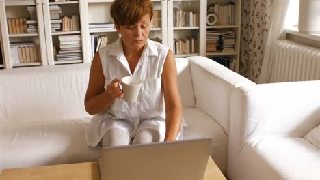 Ältere-Frau-Benutzt-Laptop,-Während-Sie-Im-Wohnzimmer-Kaffee-Trinkt