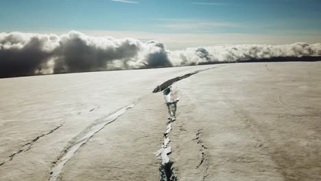 aerial landscape view of a huge crack on the ice surface of an icelandic glacier, over the clouds, on a bright sunny day