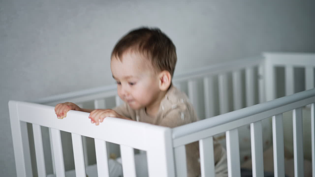 Un bambino carino e adorabile cammina nella sua culla bianca. Il bambino giocoso salta per scuotere il lettino. Bambino a casa.