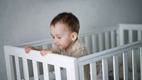cute lovely boy walks in his white crib. playful child jumps to shake the bed. baby at home.