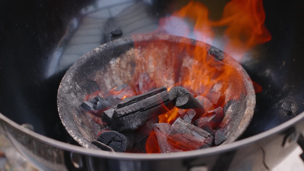 A mesmerizing slow-motion close-up of red-hot burning wood and charcoal embers glowing with intense heat and flickering flames inside a barbecue grill, ready for cooking