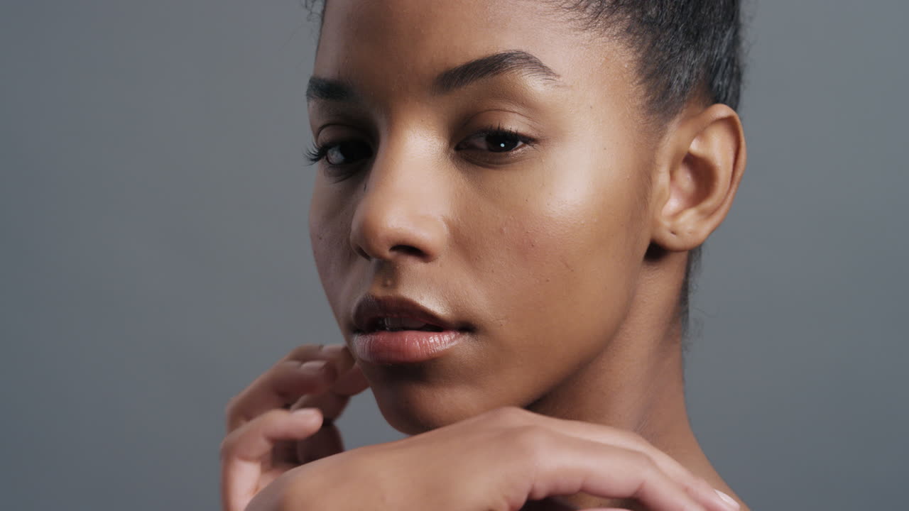 retrato de cerca hermosa mujer afroamericana tocando la cara con las manos acariciando los hombros desnudos disfrutando de una piel suave y saludable belleza natural perfecta sobre un fondo gris