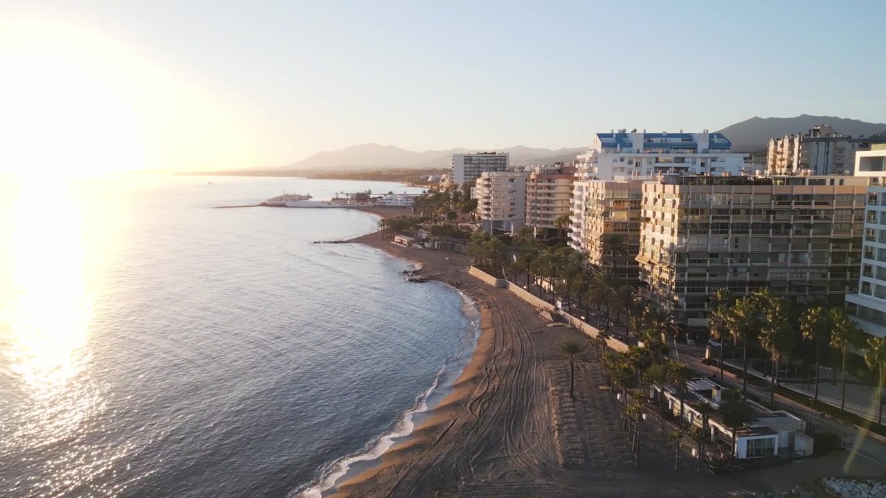 Splendida vista aerea mozzafiato al tramonto sulla lussuosa costa e spiaggia di Marbella, con il lungomare fiancheggiato da palme che risplende e un caldo bagliore solare attraverso l'obiettivo.