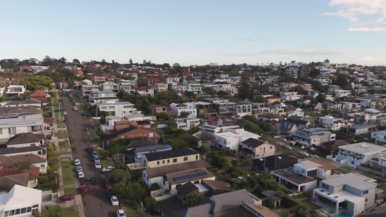 Long Reverse Aerial Drone Shot Over Sydney Coastal Homes – Revealing Oceanfront Cliffs, Crashing Waves, Blue Water, Rooftops, and Morning Sky in NSW, Australia