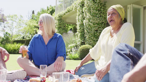 Feliz-Mujer-Mayor-Birracial-Hablando-Con-Diversos-Amigos-En-Un-Picnic-En-Un-Jardín-Soleado,-Cámara-Lenta