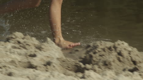 Female-legs-in-skirt-run-barefoot-along-water-on-sandy-beach,-slow-mo