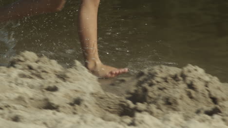 female legs in skirt run barefoot along water on sandy beach, slow-mo