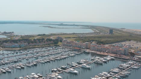 cinematic drone - aerial tracking panorama shot of a marina - port with sailing boats on a sunny day with the north sea in the background, 30p