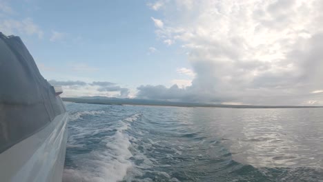 waves are being formed by the movement of the boat on a panga ride on an ocean of the galapagos islands. a bigger island is seen on the back with clouds and blue sky on top