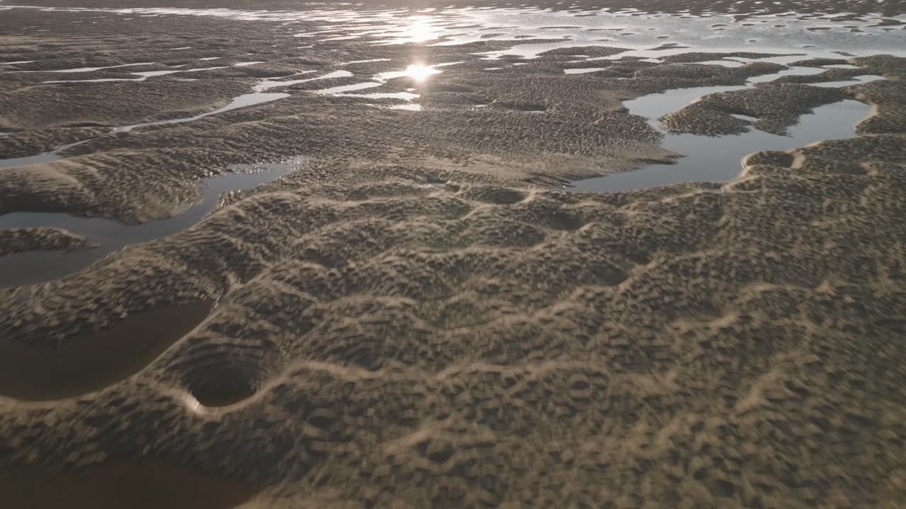 Tidal sands and seawater pools with low sun reflecting off water. Flying over sandy ripples.