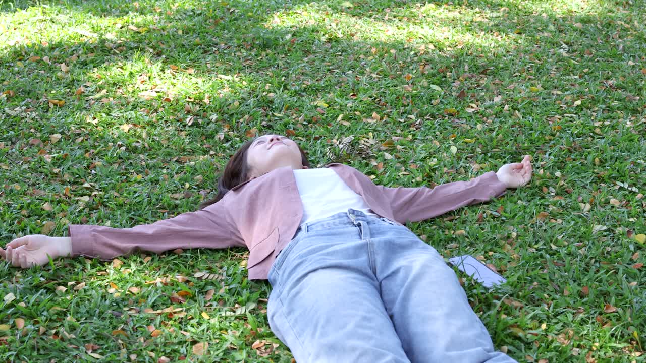 A young woman lies on green grass with arms outstretched during a sunny day