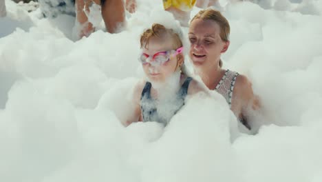 funful children's holidays with the whole family, a young active woman with her little daughter are having fun frolicking on a foam party at the seaside