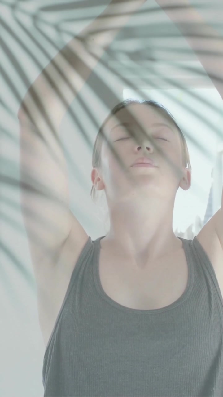 Animation of green palm leaves over caucasian woman practicing yoga meditation in sunny room