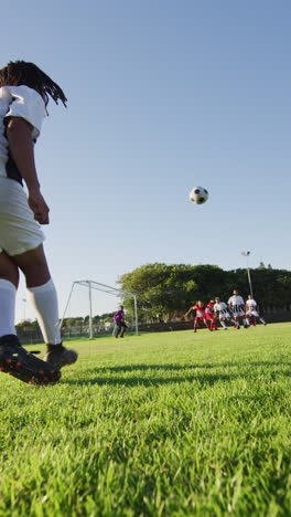 video vertical de un jugador de fútbol biracial en el campo pateando la pelota