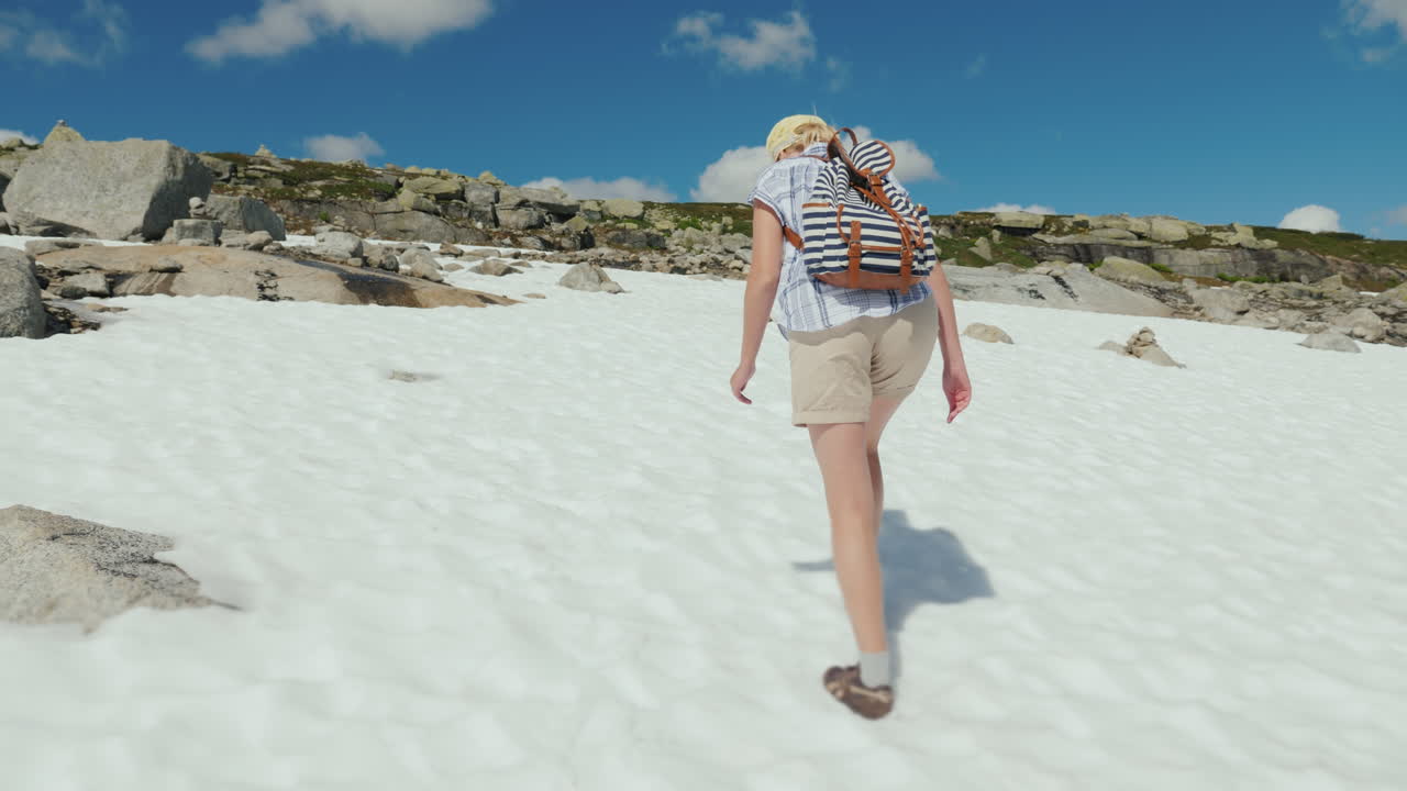 한 여자가 밖에 산에서 눈 위를 걷고 있습니다. 더운 여름입니다. 눈이 녹지 않았습니다.